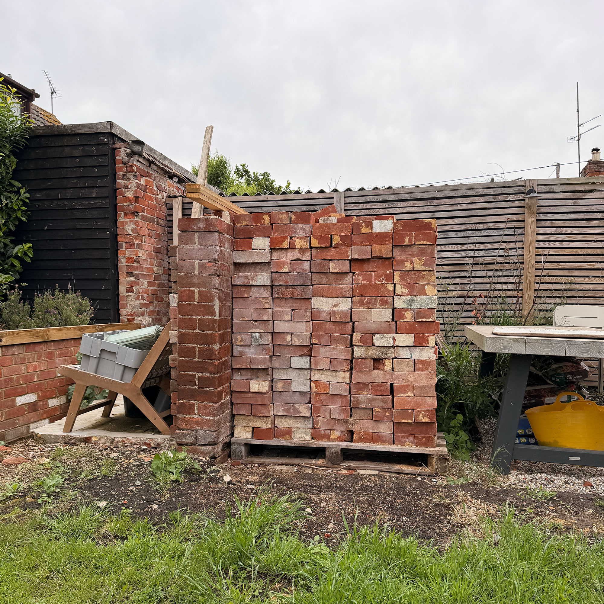 Large piles of bricks in front of slatted wooden fence in garden