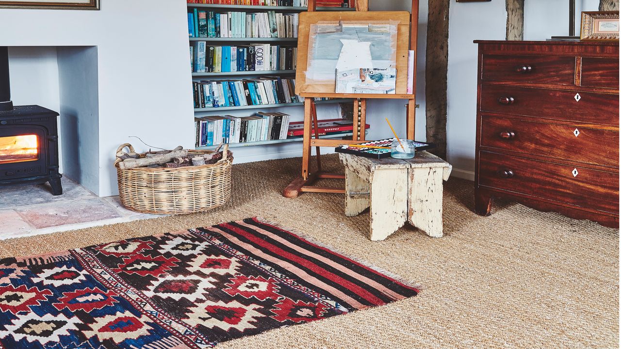 beige carpet with wooden chest of drawers, painting easel, wood burning stove, bookcase with books