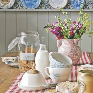 A dining table with breakfast foods, a gingham tablecloth and a vase of fresh flowers