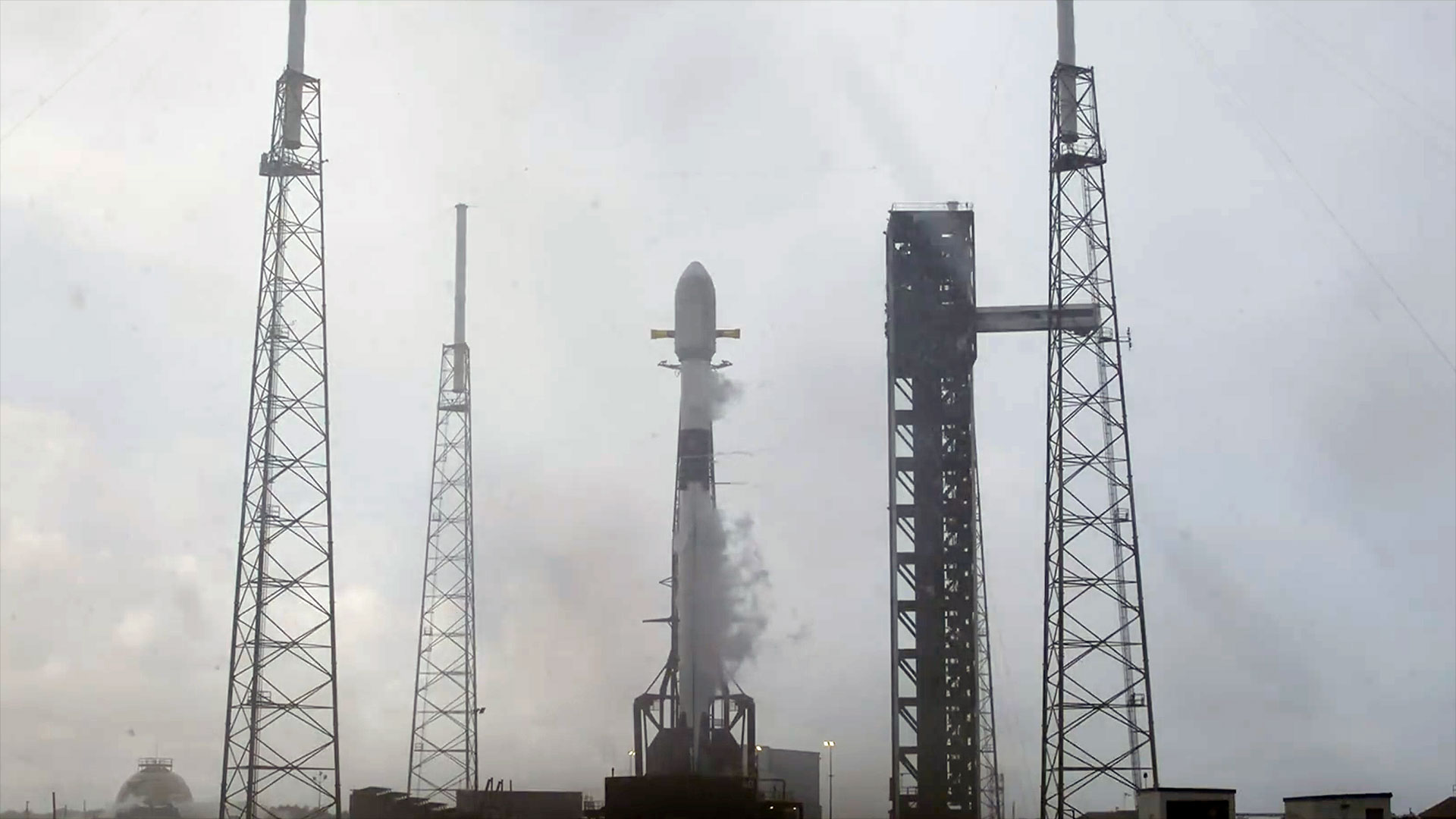 a white and black rocket sits on a launch pad awaiting its lift off under an overcast sky.