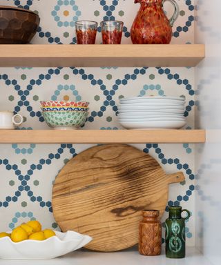 A white kitchen with white and blue patterned tiles and wooden floating shelves