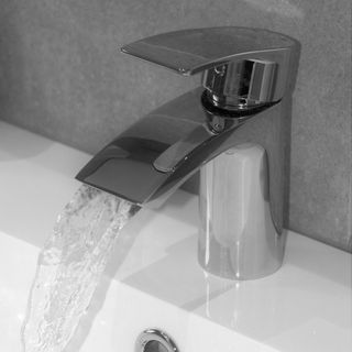 Silver mixer tap with running water into white sink