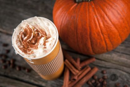 Image of a pumpkin spice latte next to a pile of cinnamon sticks and an orange pumpkin.