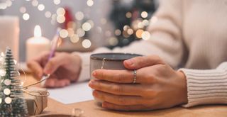 Person with a piece of papaer and pen sat in front of fairy lights to show writing a to-do list for Christmas hosting tips