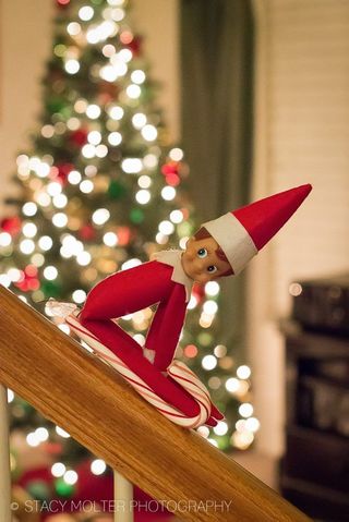 An elf figurine on a banister with candy cane acting as sled.