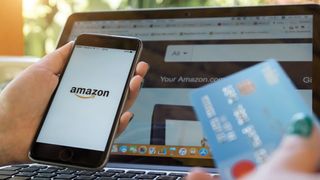 Woman in front of a laptop displaying the Amazon website while holding a phone and credit card