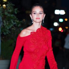 a paparazzi photo of a woman in a bright red dress and diamond earrings with her hair pulled back into a bun