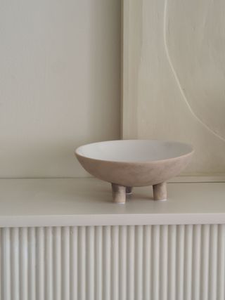 a beige bowl on a white fireplace with art behind