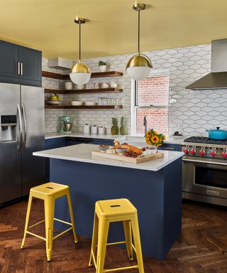 kitchen island color ideas, blue and yellow kitchen with yellow ceiling, blue island, yellow stools, white tiled walls, open shelving, white countertops