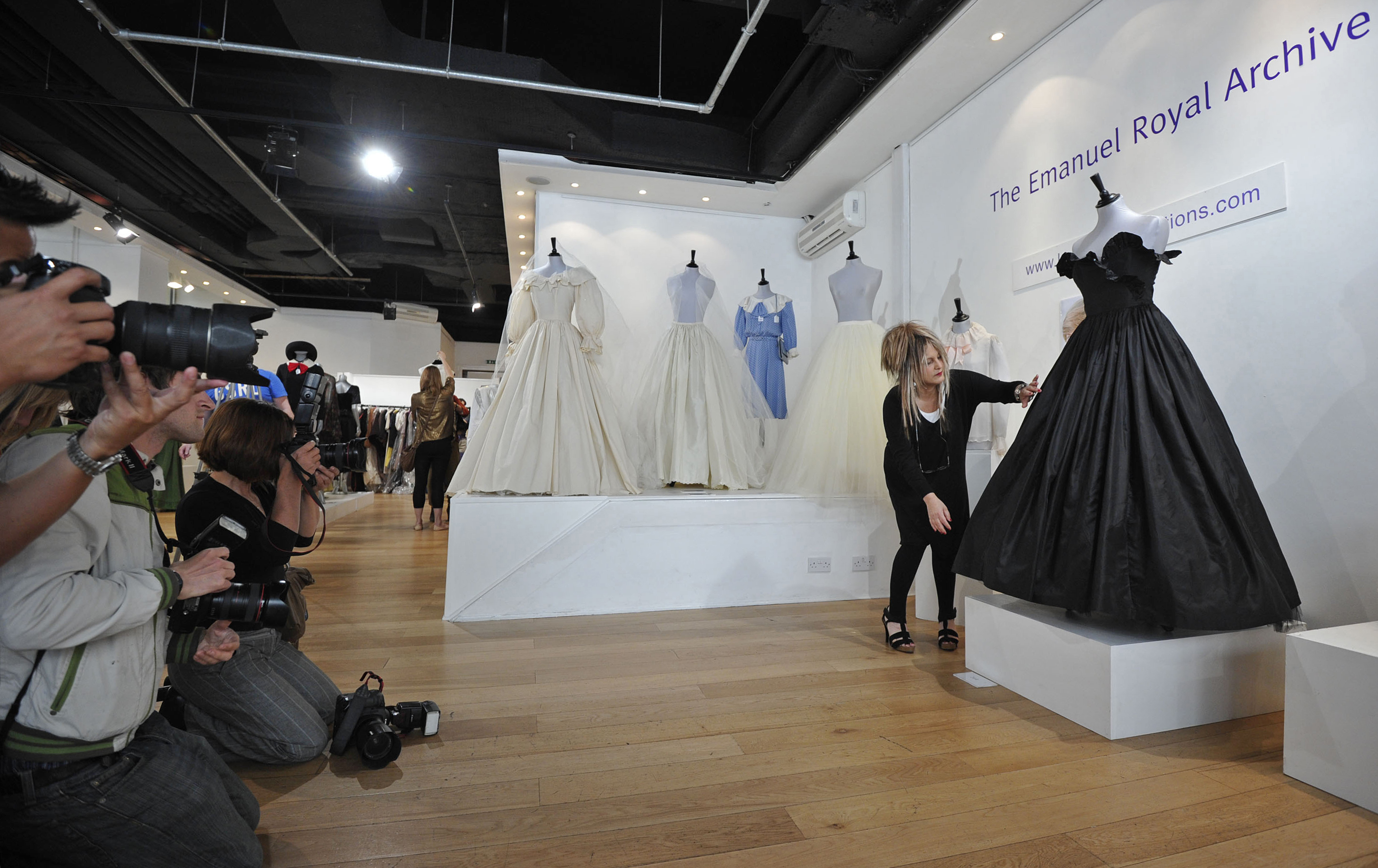 Elizabeth Emanuel arranging the skirt of Princess Diana's black gown at an exhibit