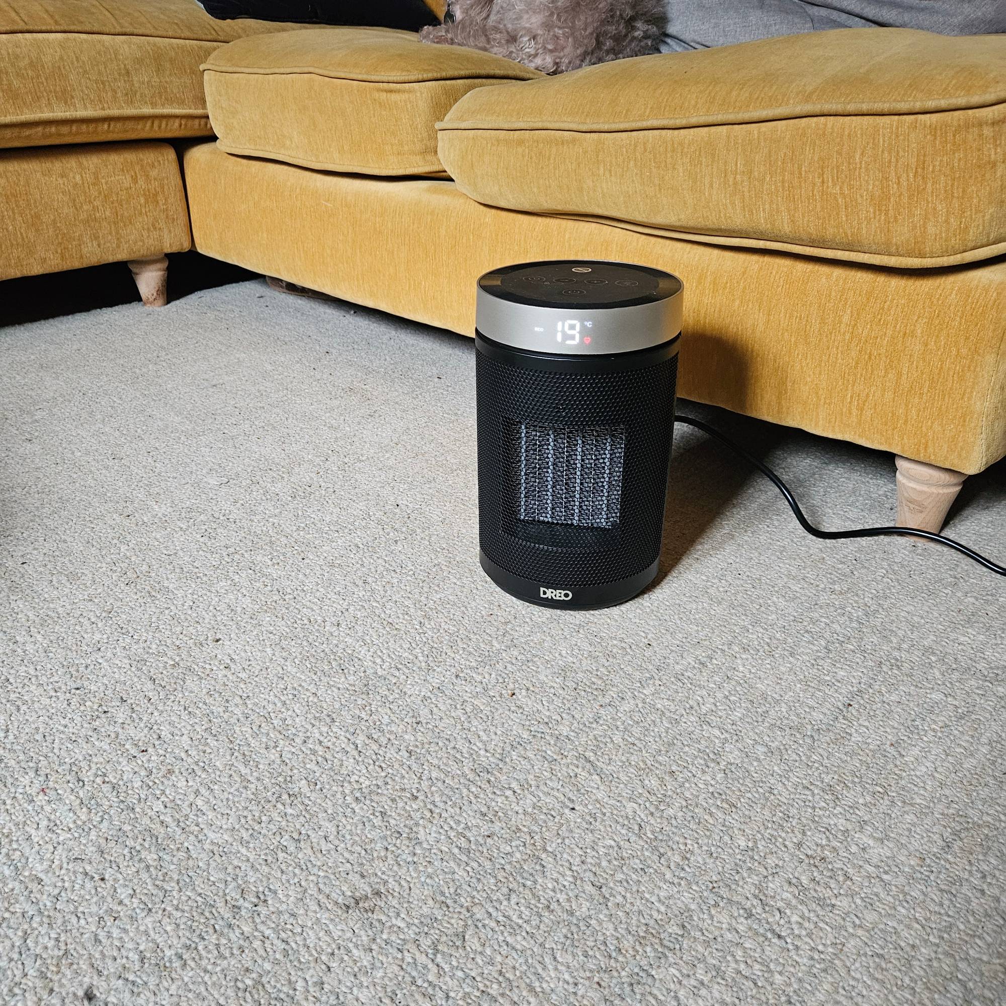 dreo fan heater turned on next to yellow sofa in living room