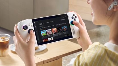 Player holding white ROG Xbox Ally X handheld with table in backdrop and iced coffee.