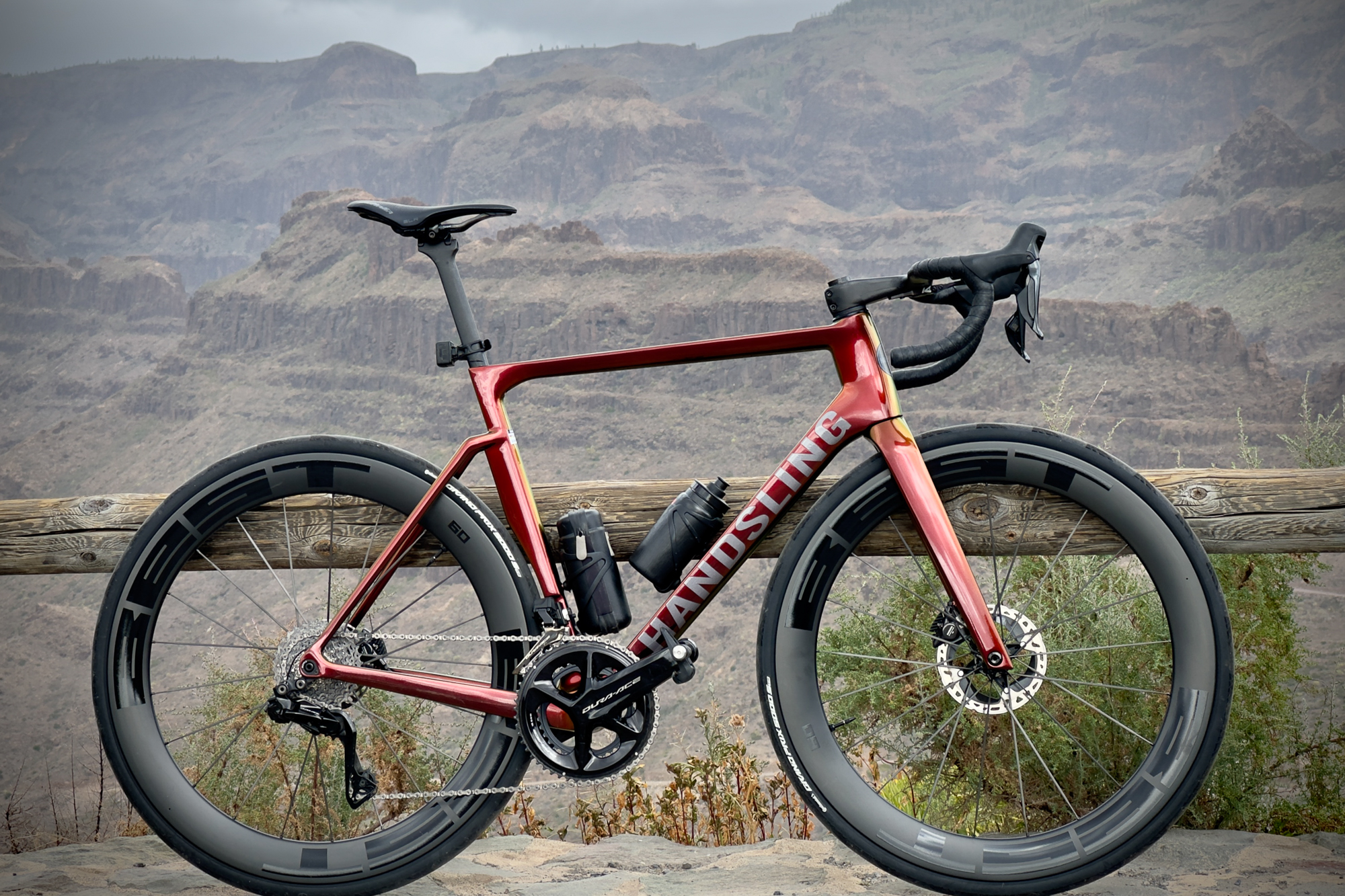 an orange bike leaning against a wooden rail with hills in the background