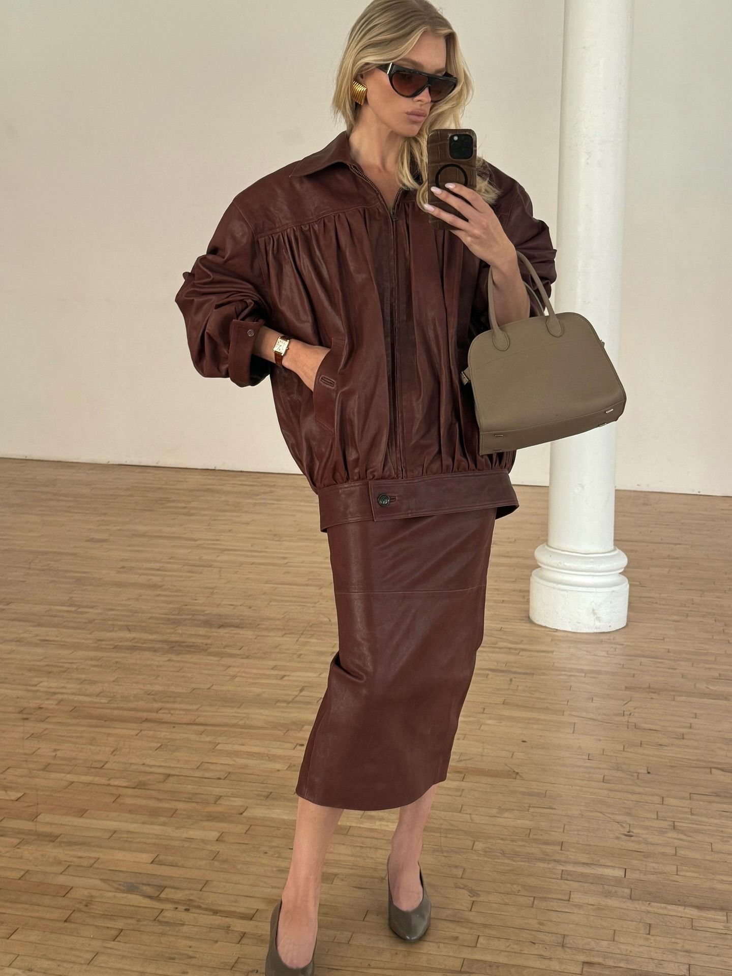 Model @hoskelsa takes a mirror selfie wearing a brown leather skirt with a brown leather jacket a mid heel pumps