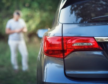 A car in the foreground with a middle aged man standing behind it.