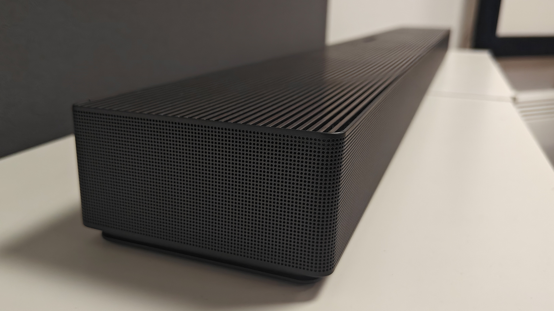 Samsung HW-QS90H Dolby Atmos soundbar on white shelving unit seen from left side