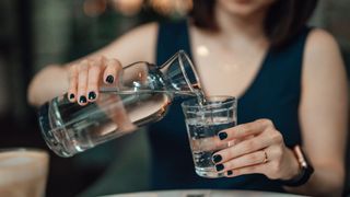 Woman pouring a glass of water from a glass bottle to rehydrate during heatwave