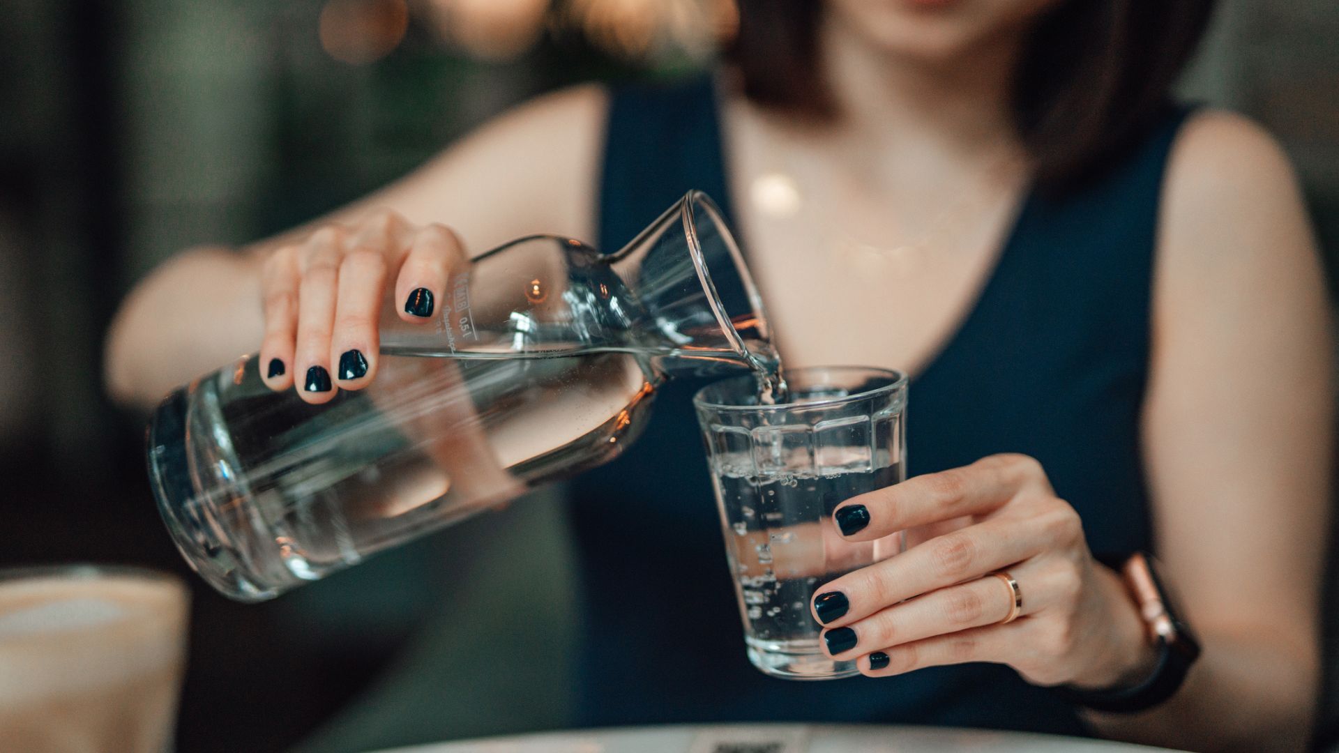 Žena nalévá sklenici vody ze skleněné láhve k rehydrataci během vlny veder