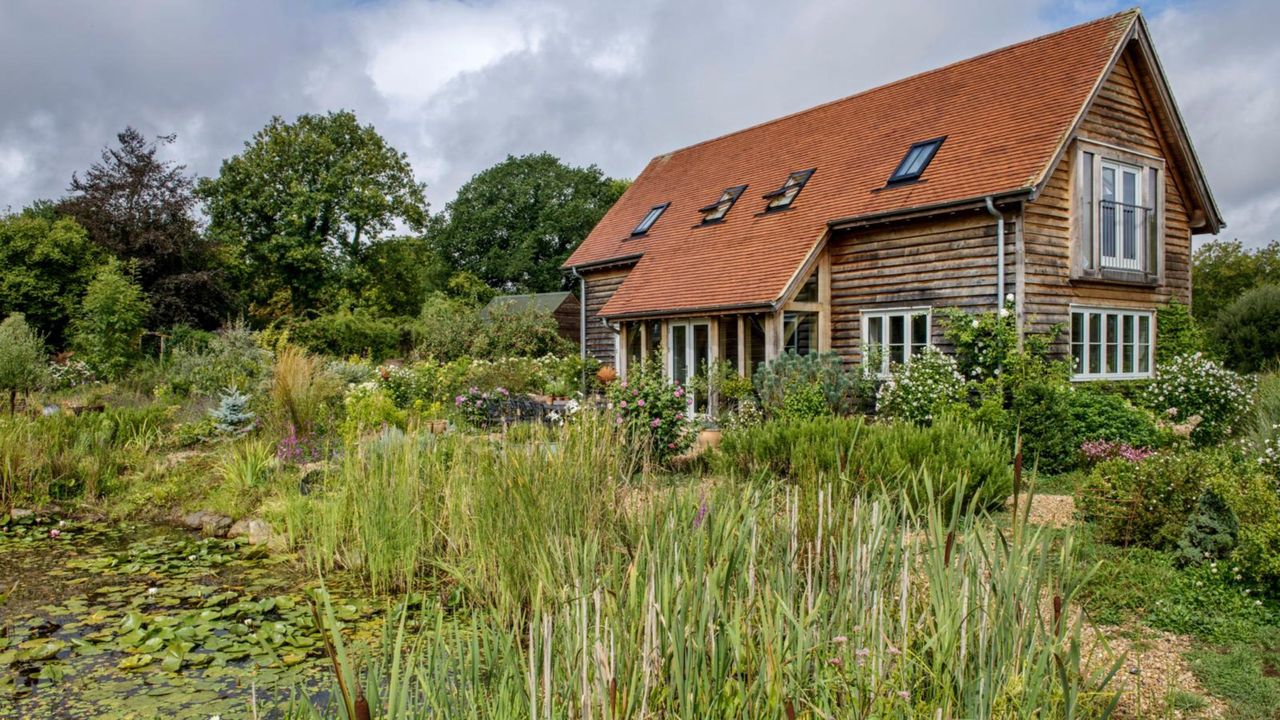  Exterior of a timber clad, oak framed house with lawn and flower beds. A new build oak framed two bedroom house in the New Forest in Hampshire, home of Elizabeth and Derek Sandeman