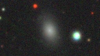 A photo of stars and galaxies in deep space, with a white smudge showing the runaway dwarf galaxy