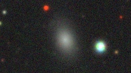 A photo of stars and galaxies in deep space, with a white smudge showing the runaway dwarf galaxy