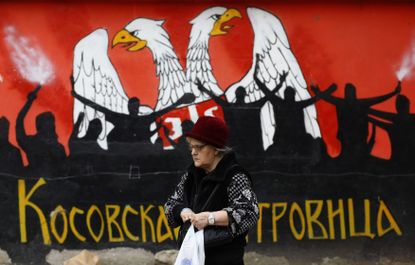 A woman walks in front of a mural depicting part of the Serbian flag.
