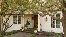 a white painted brick house with trees and potted plants on the front step