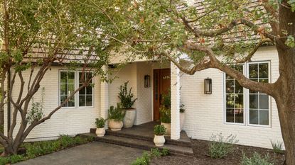 a white painted brick house with trees and potted plants on the front step
