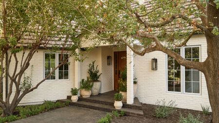 a white painted brick house with trees and potted plants on the front step