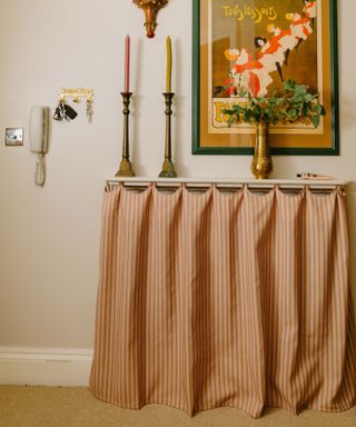 pink and white curtain covering radiator with brass candlesticks