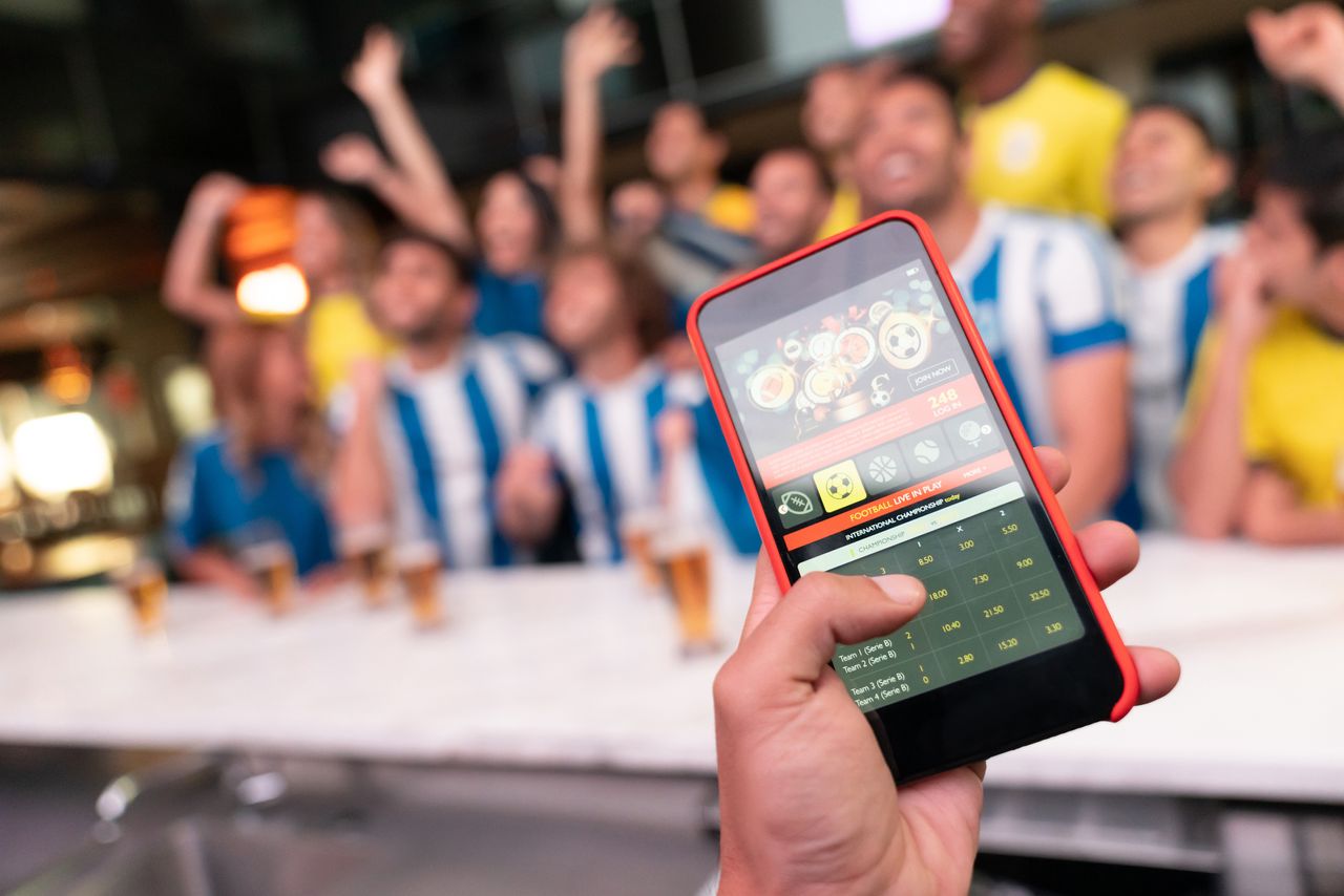 A man holding a cell phone while winning an online bet on a football game.