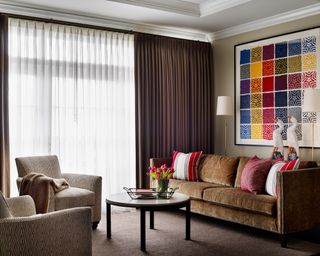 Living room with brown velvet sofa facing two armchairs, coffee table and colorful artwork on wall