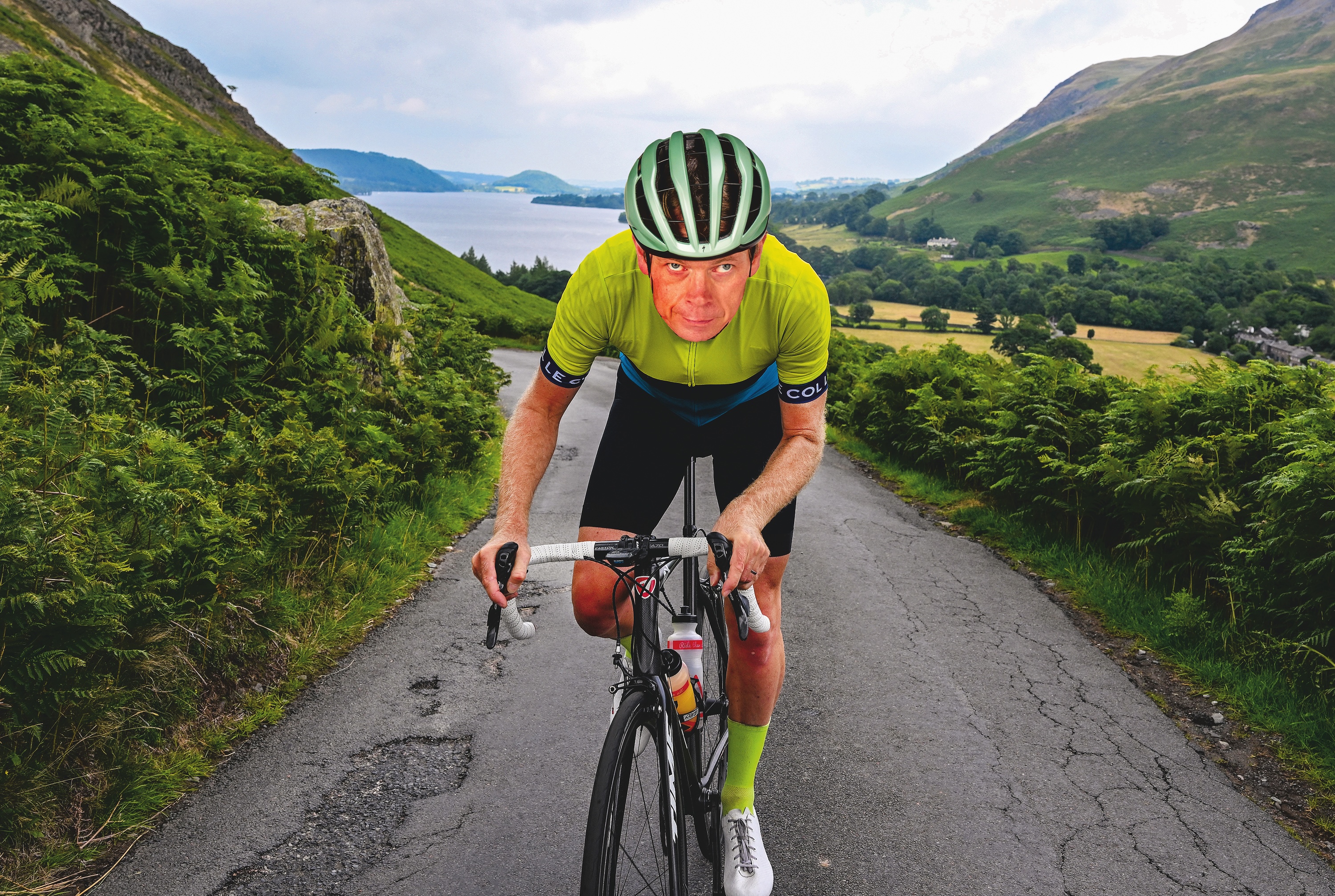 A man cycles up a mountain road, in a green jersey