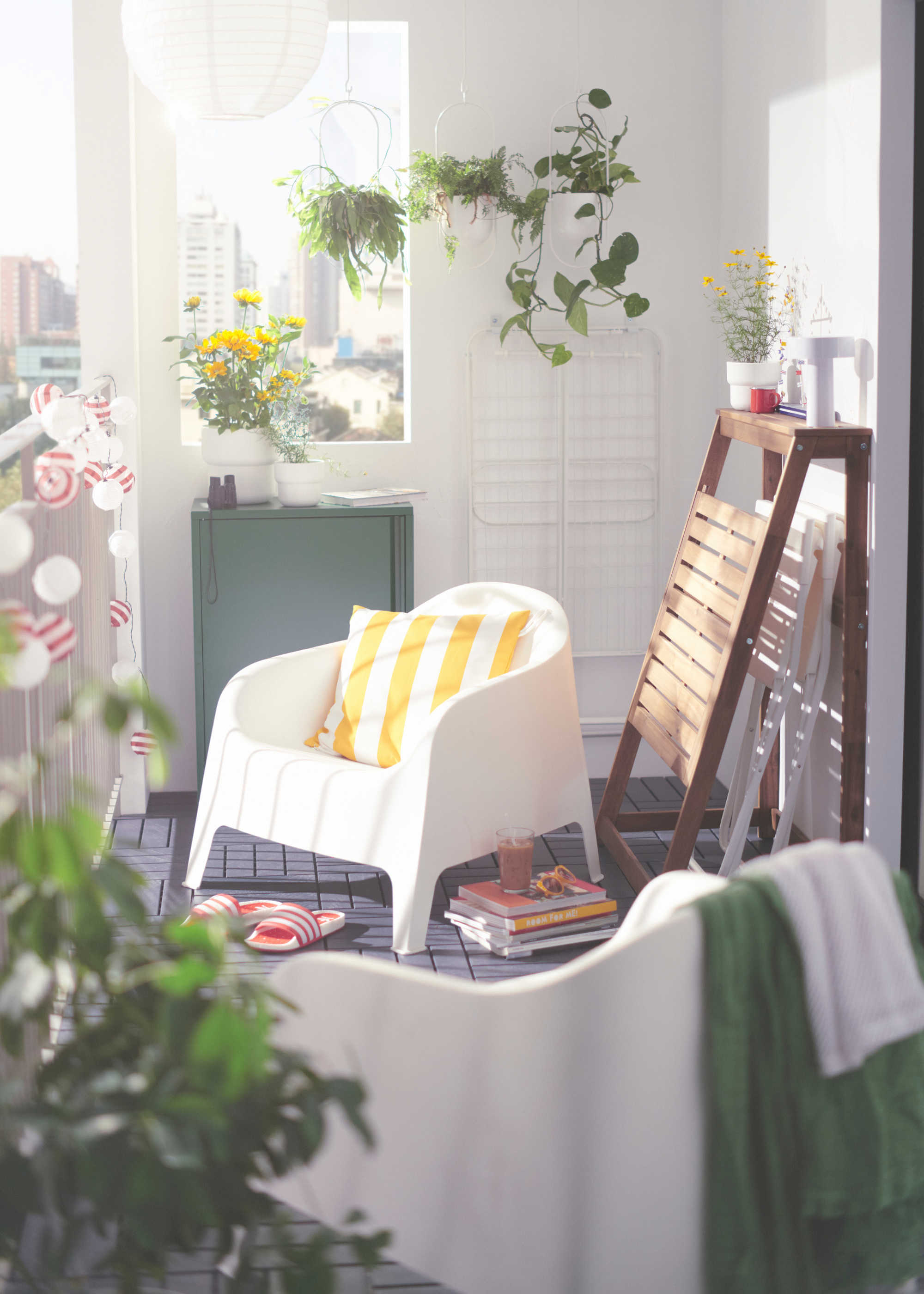 IKEA DJUPON Outdoor Folding Table folded away on a balcony with two white folding chairs inside, with a white chair next to it with a white and yellow striped cushion on it