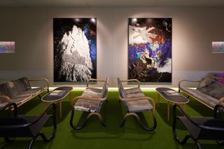 Alternative view of the Netjets VIP lounge at Art Basel featuring light coloured wall panels, green flooring, wall art, grey patterned seating, black chairs and oval shaped tables