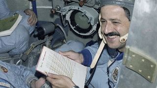 a smiling man with a mustache holds a clipboard