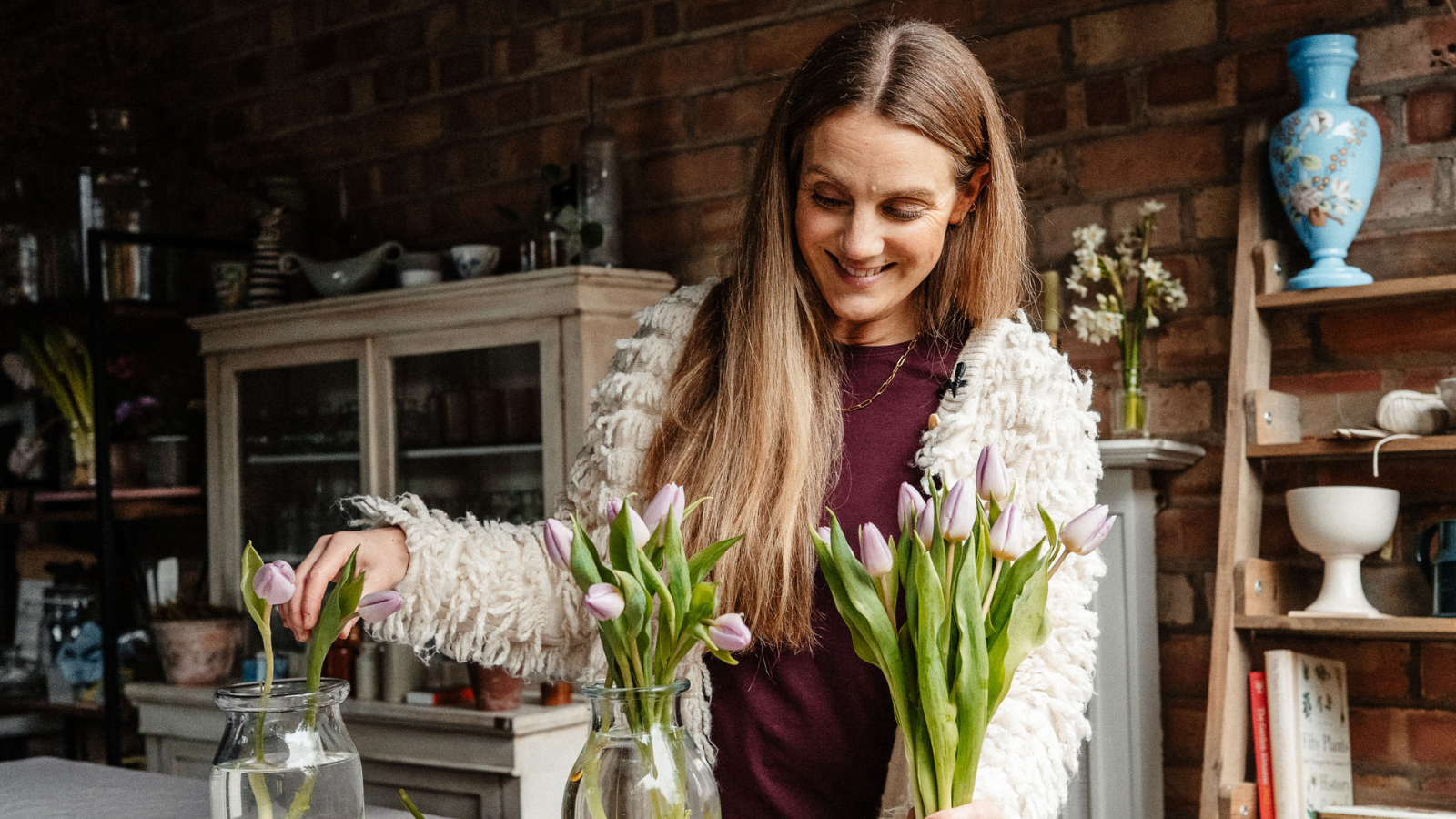 Woman in a floristry workshop placing tulip stems into a vase and holding a bunch in her other hand