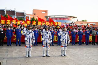 Three Shenzhou 16 astronauts waving with a crowd of spectators with Chinese flags behind them