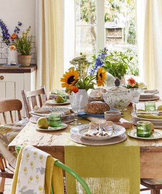A dining table decor idea with yellow runner on farmhouse style table with rattan placemats and summer flower arrangement