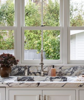 kitchen sink ideas, detail of kitchen sink with marble countertop, window view of garden, white units, chrome faucet,