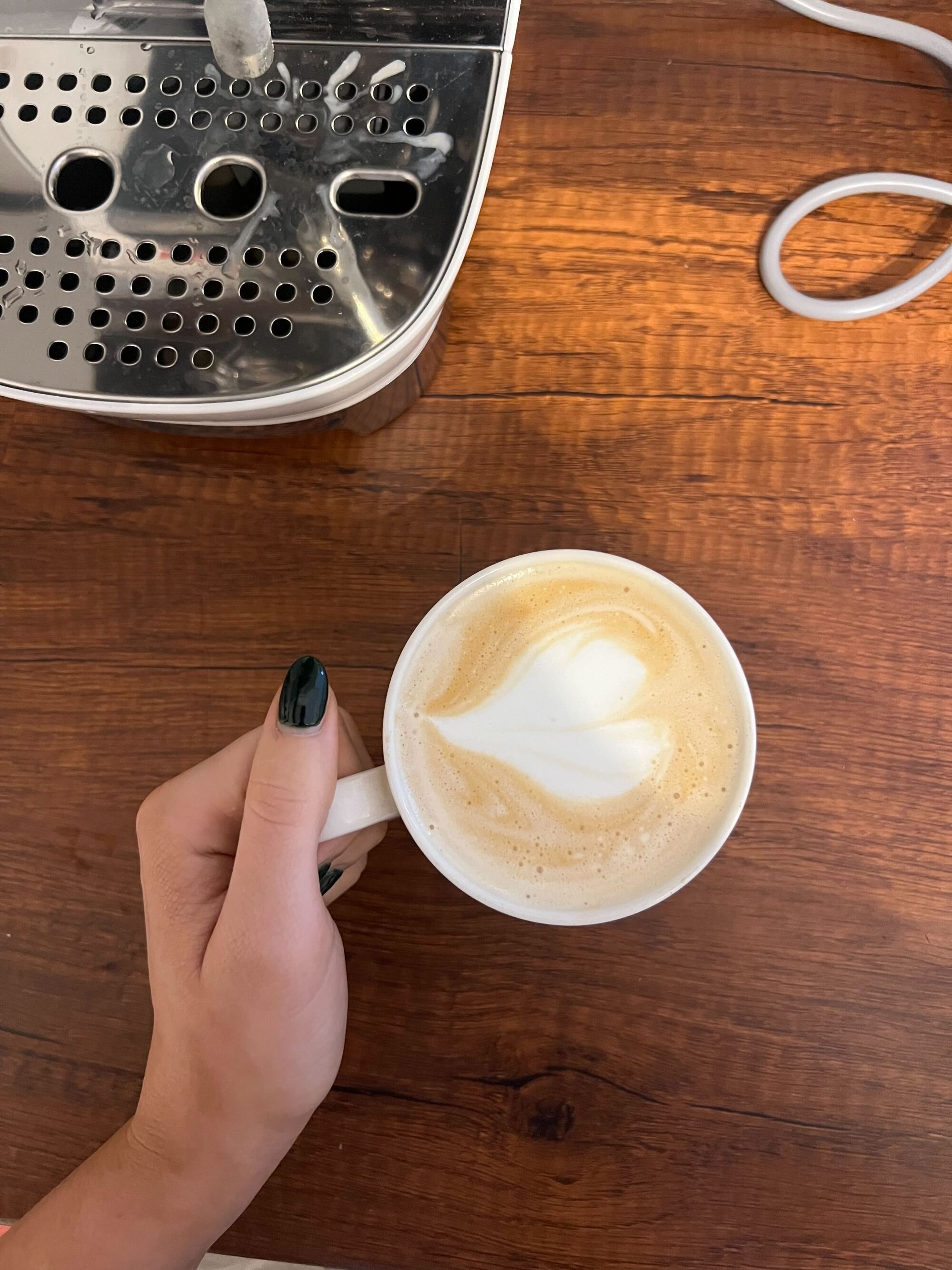 Image of a hand holding a mug with a latte in it on a wooden countertop.