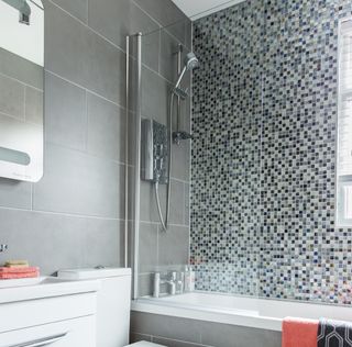 bathroom with grey and designed tile wall and bathtub