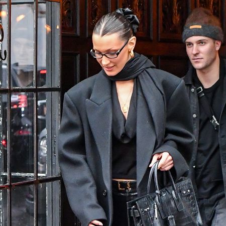 Bella Hadid wears a black wool coat, black blouse, black leather pants, black boots, and black hermes bag.