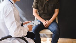 Man sitting with his hands over his crotch talks to a doctor