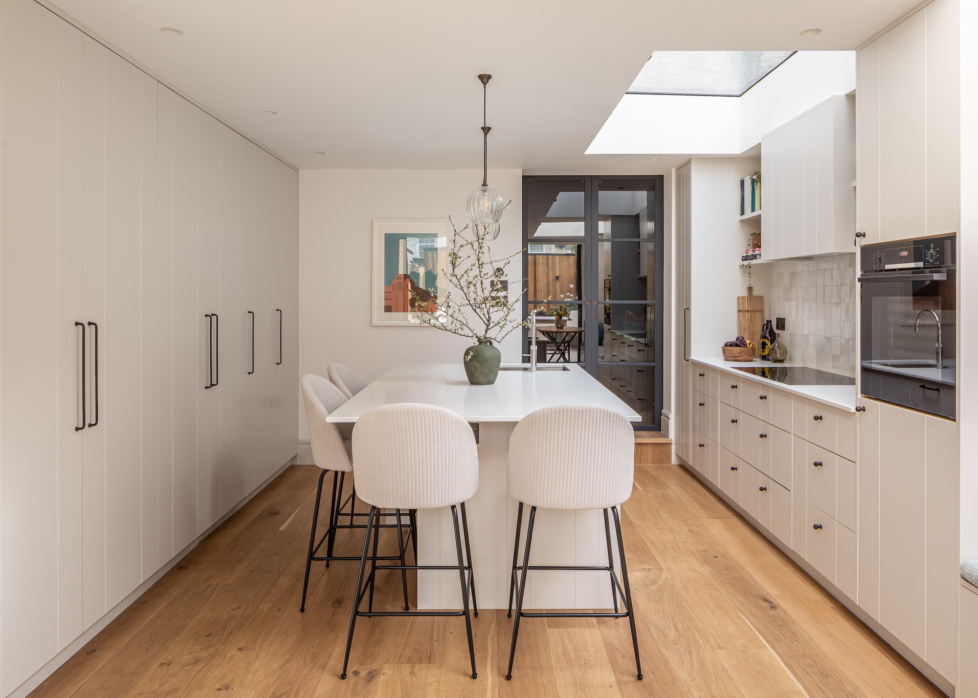 A simple white galley kitchen consisting of floor to ceiling cupboards one one side and a mix of wall and base units on the show, shown with a central island unit