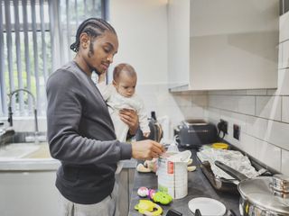 Father holding baby while mixing up baby formula in kitchen