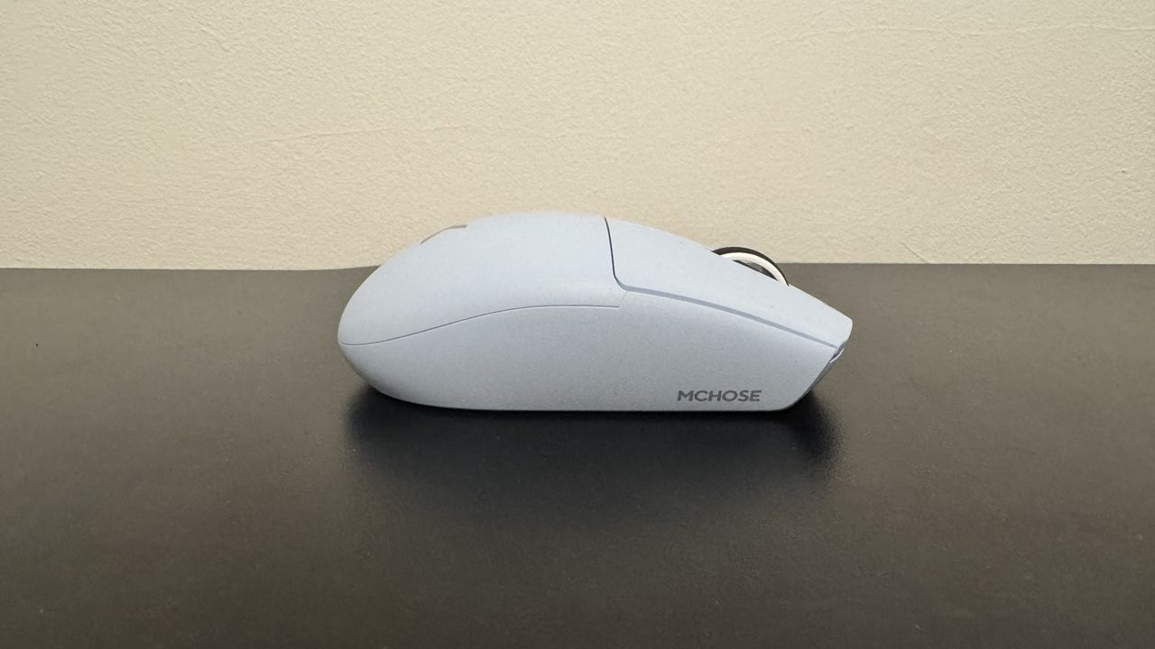 The blue Mchose G3 V2 gaming mouse from the right side on a black desk