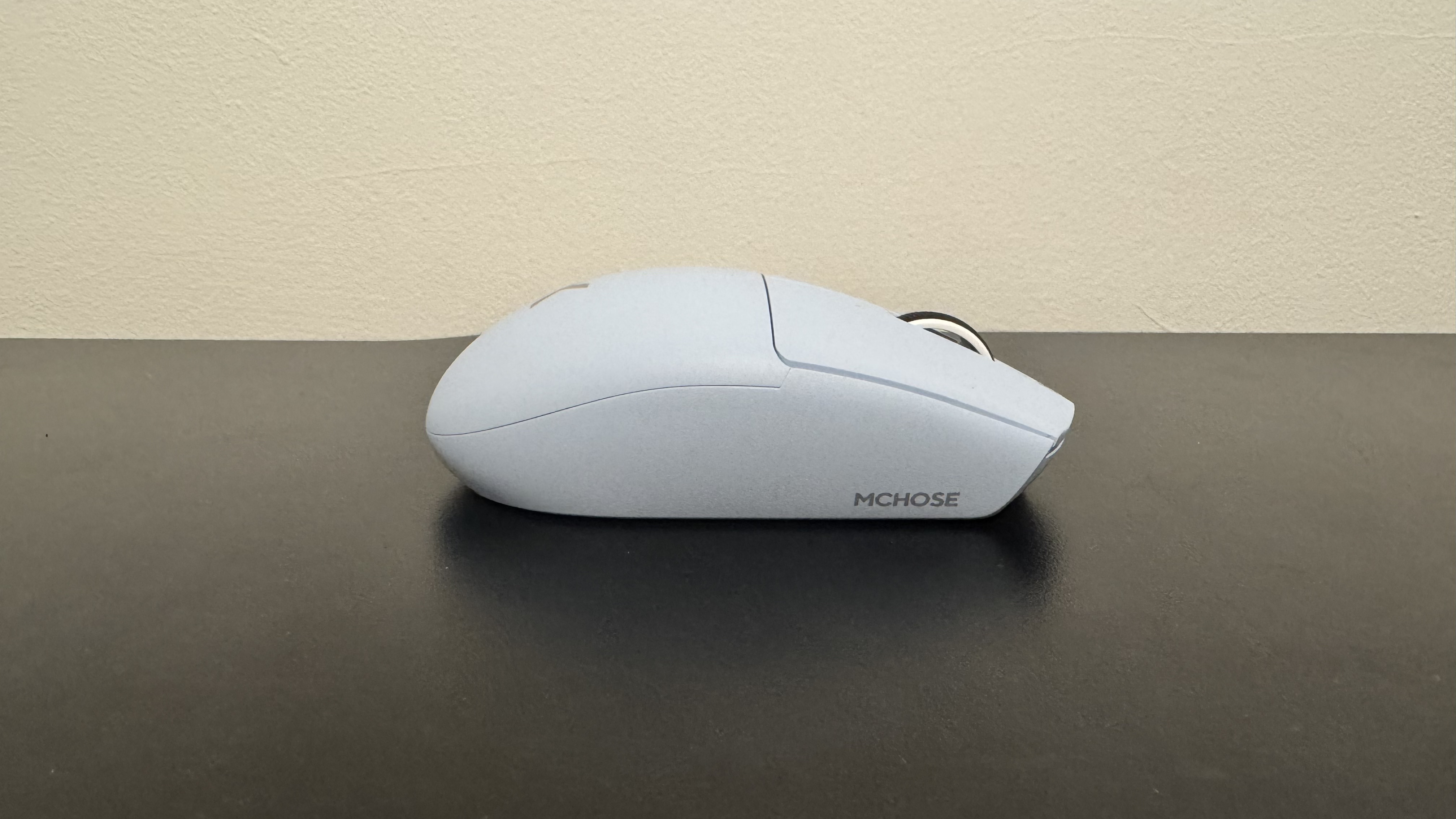 The blue Mchose G3 V2 gaming mouse from the right side on a black desk