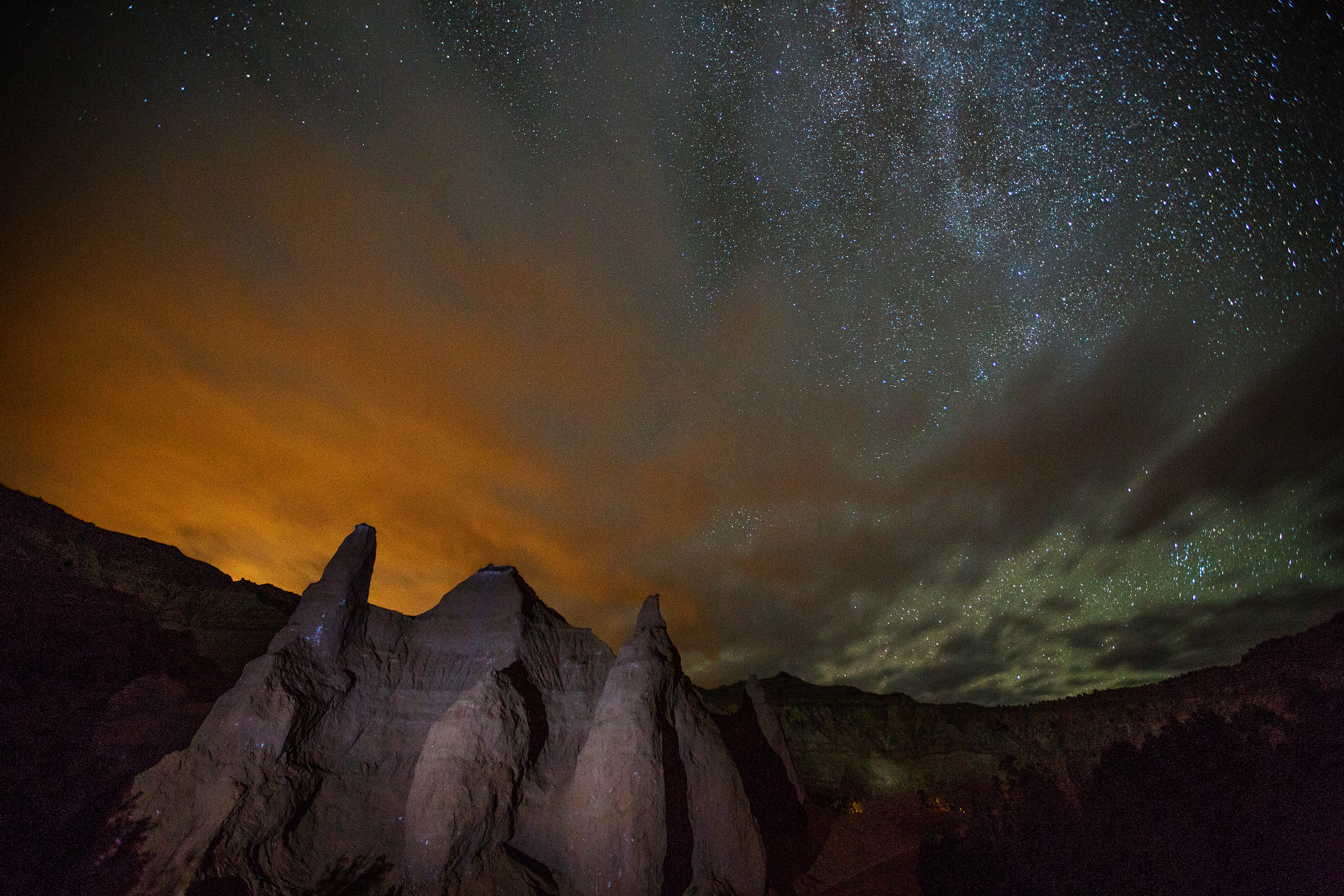 partly cloudy sky with stars on the right side of the image and a rock formation in the foreground.