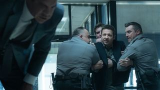 Clayton Cardenas as Torres bending down and Jeremy Renner as Mike McLusky being pulled away by police officers.